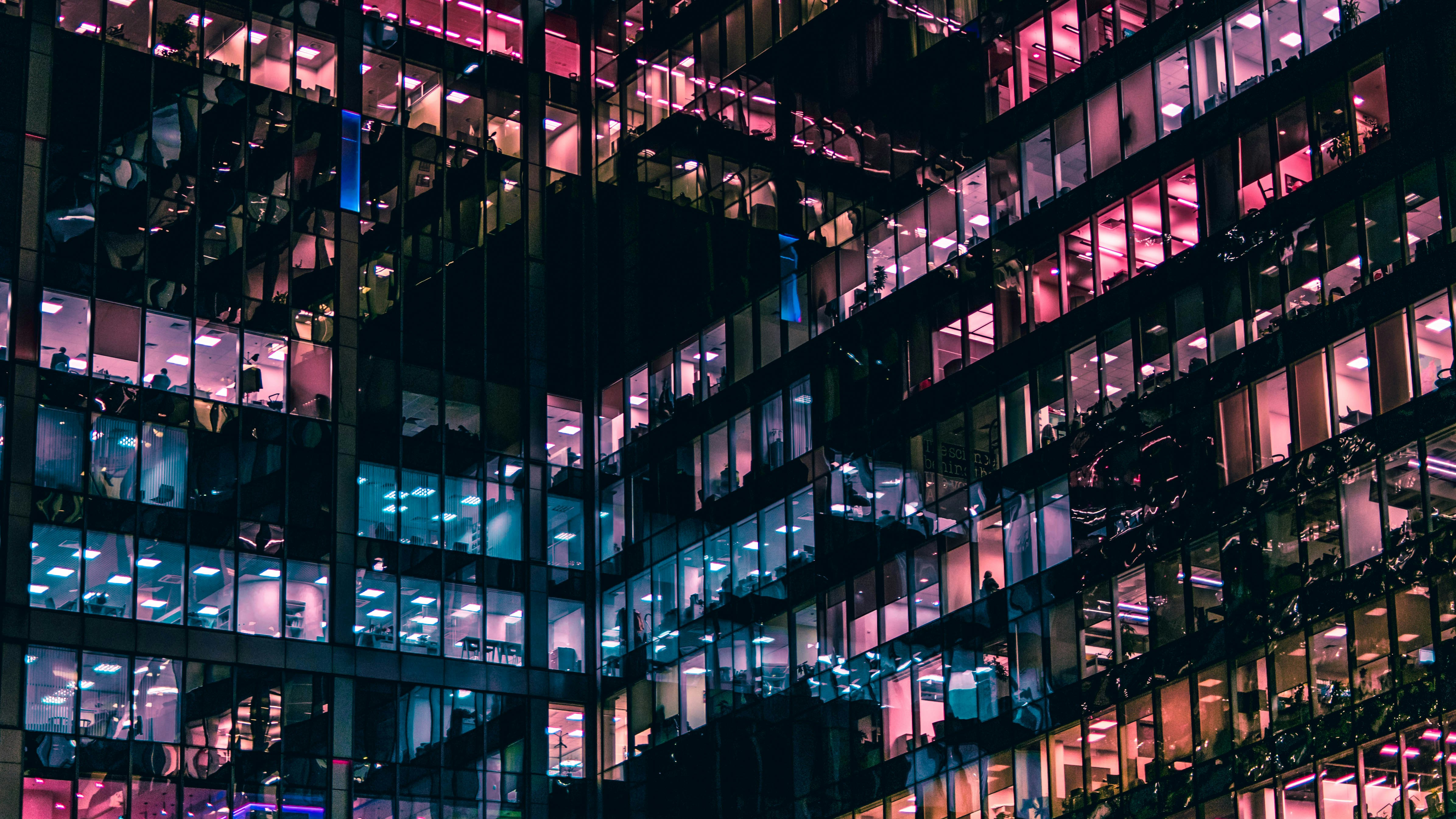 Windows on a city skyscraper are lit up in a range of colours, from bright pinks to cool blues.