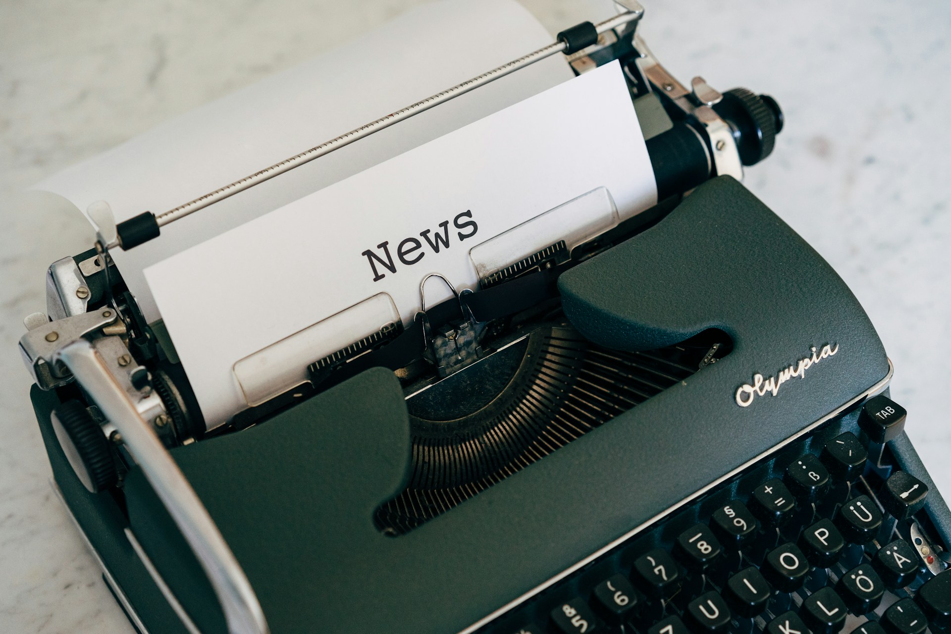 A typewriter with a single sheet of paper fed through it. On the paper it reads 'News'.